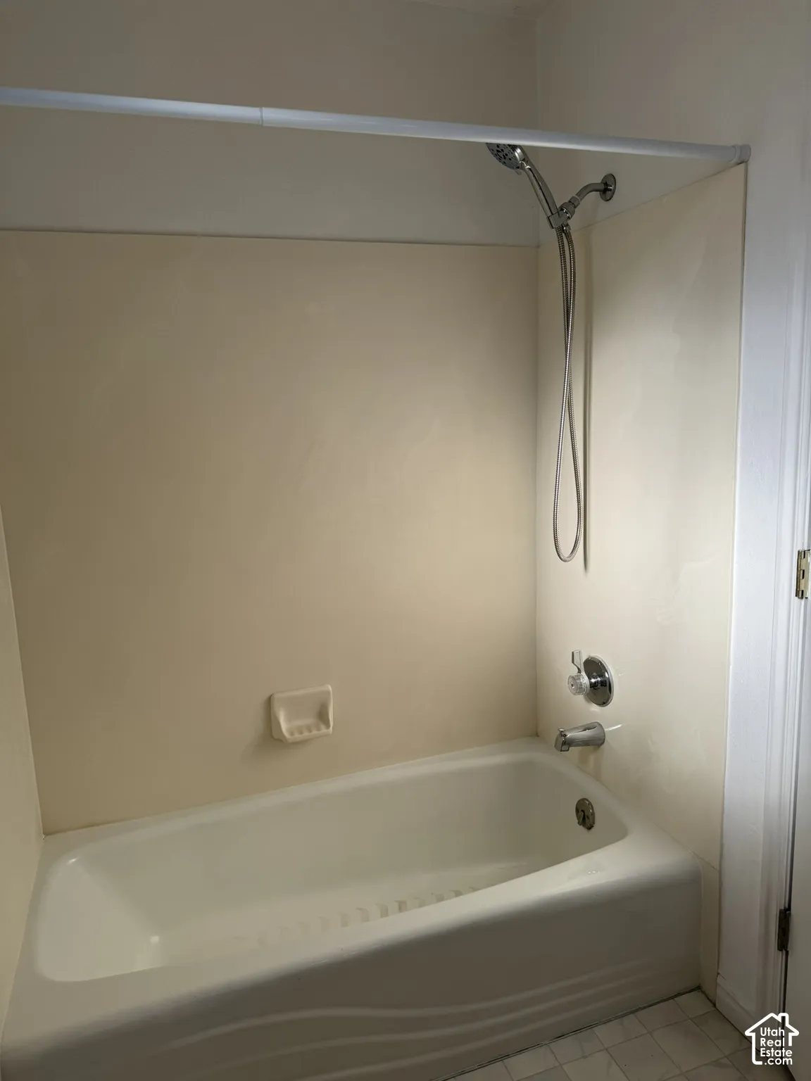 Bathtub with integrated shower surround, chrome showerhead and faucet, and white tile flooring
