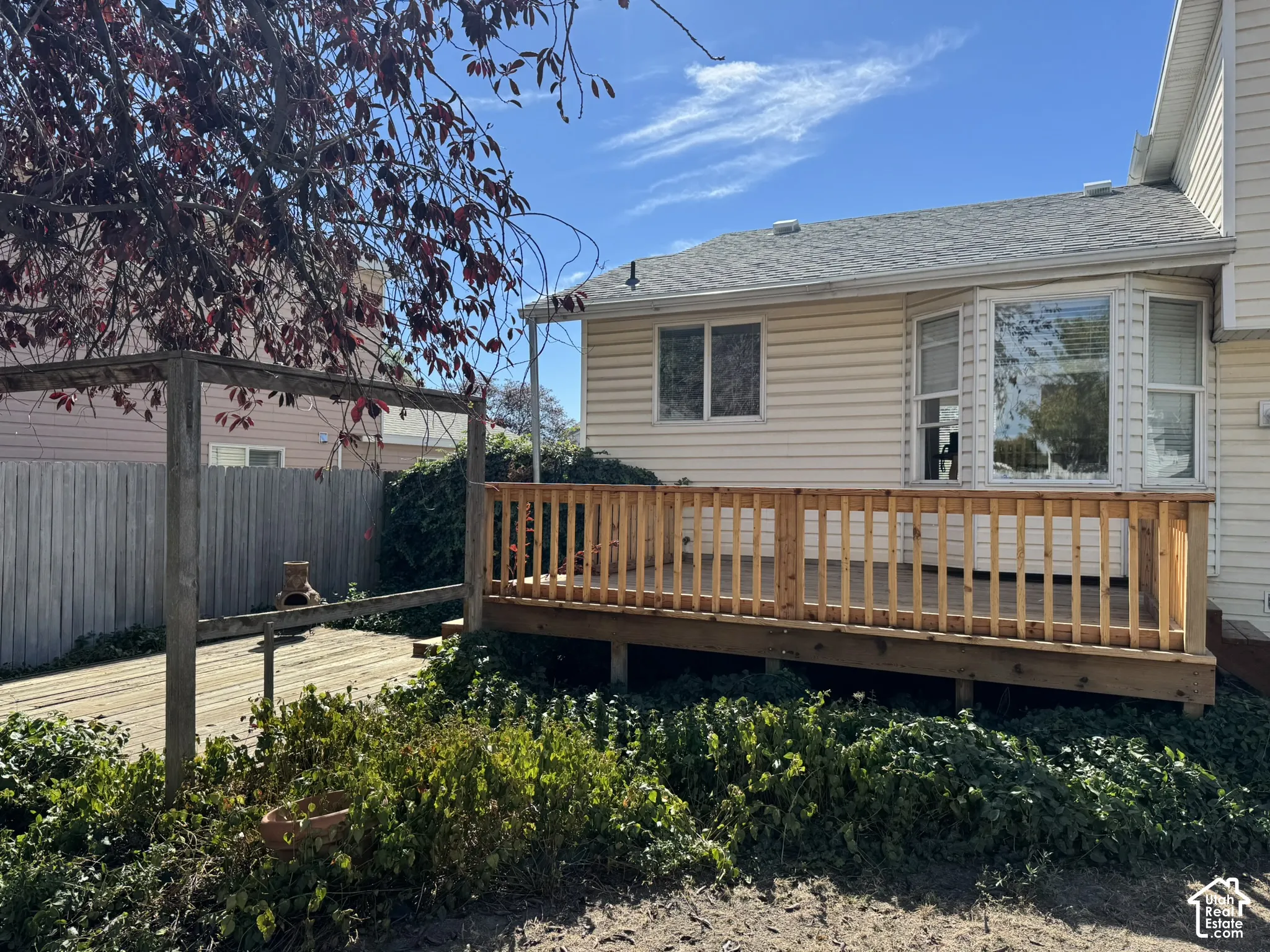 Rear wood deck with natural wood railing, bay window, light-colored siding, and a partial pergola structure