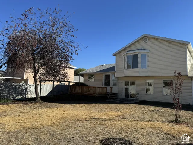 Expansive backyard featuring a mature tree, wooden decking, and vinyl siding exterior