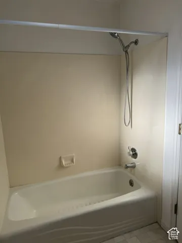 Bathtub with integrated shower surround, chrome showerhead and faucet, and white tile flooring