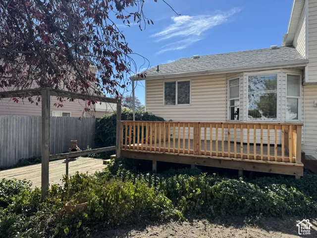 Rear wood deck with natural wood railing, bay window, light-colored siding, and a partial pergola structure