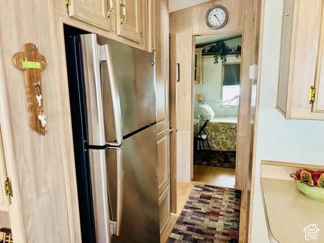 Stainless steel refrigerator, light wood-finish cabinetry, light wood-finish wall paneling, and a built-in wall clock