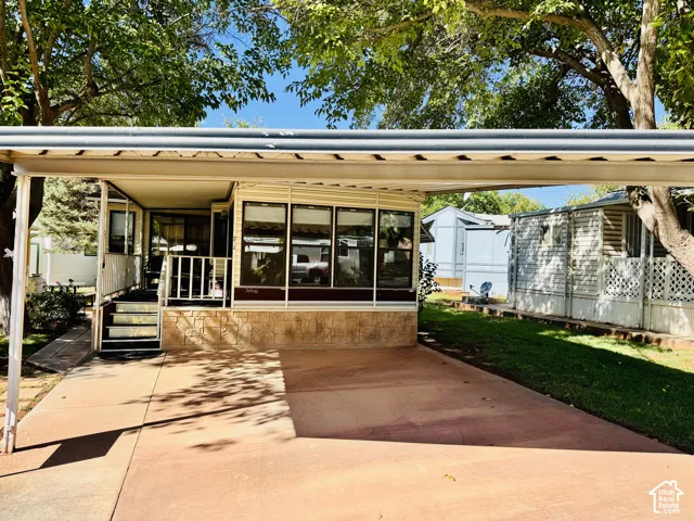 Covered carport, concrete driveway, stone veneer foundation, multiple windows, and a landscaped side yard