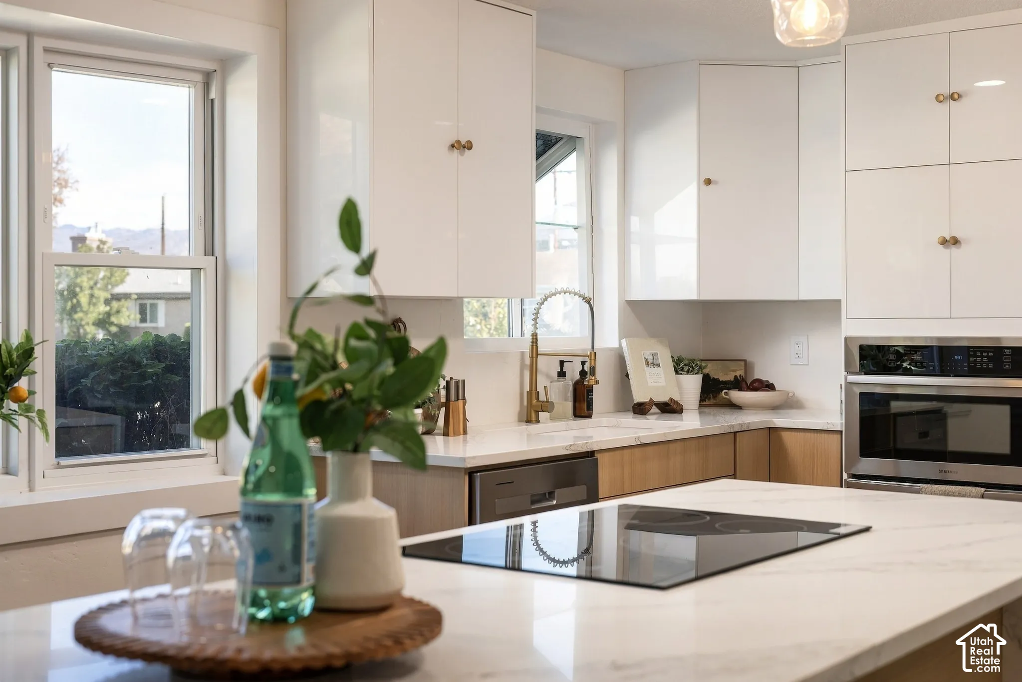 White high-gloss cabinetry, wood-finish base cabinets, integrated stainless steel microwave, built-in cooktop, and brass-finish fixtures