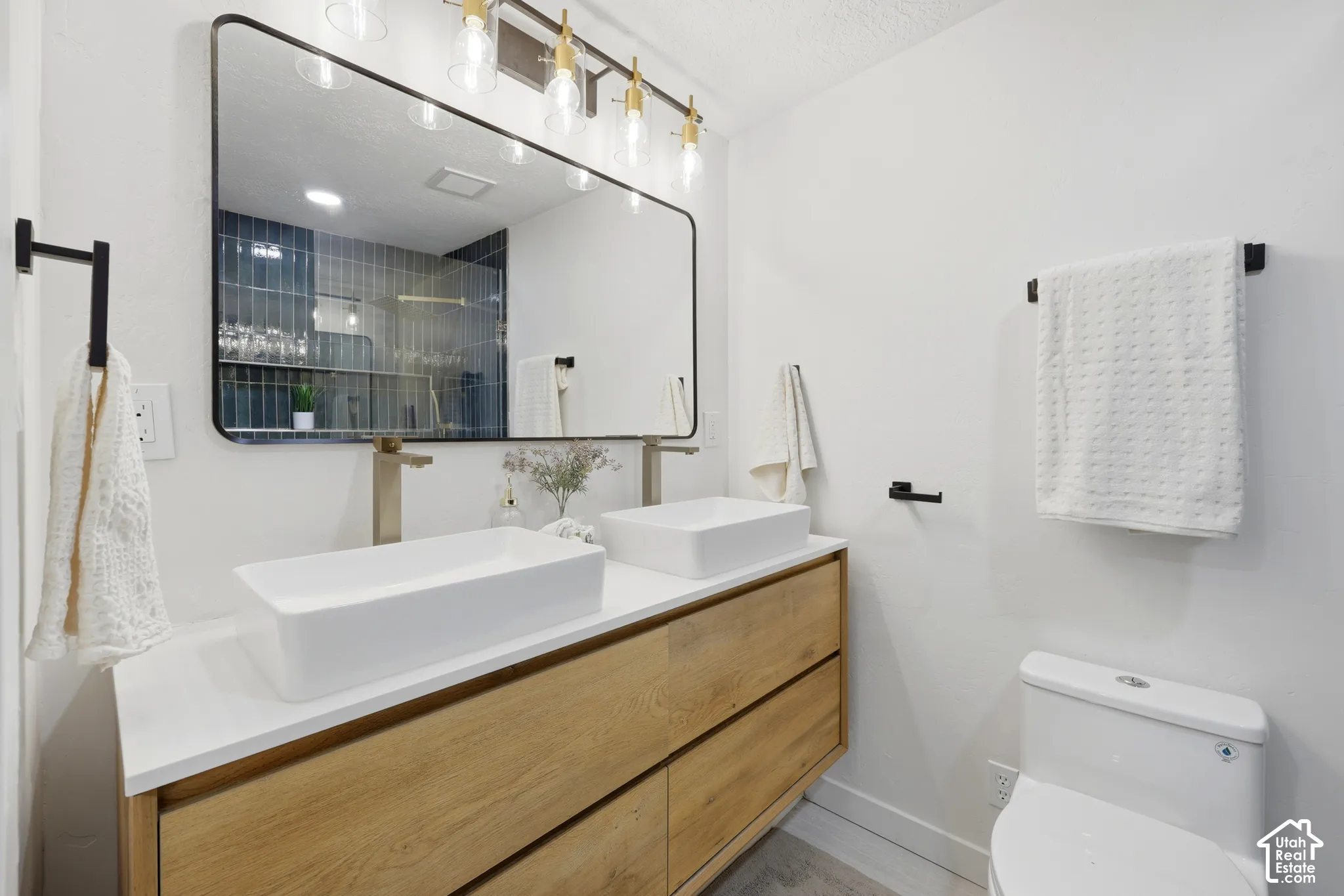 Dual rectangular vessel sinks, wood-finish vanity with drawer storage, wall-mounted brushed nickel faucets, and a large framed mirror with overhead vanity lighting