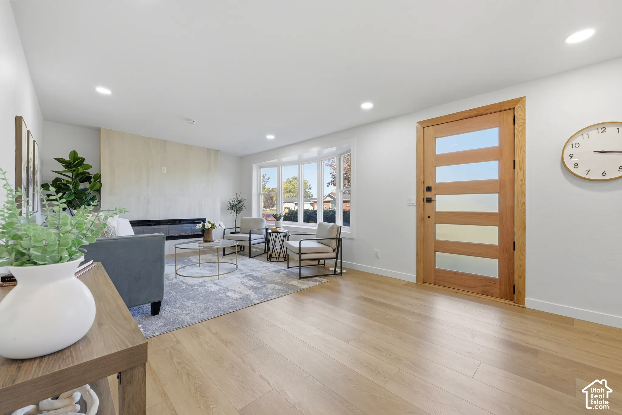 Wood-finish flooring throughout, modern wood-paneled entry door with frosted glass inserts, recessed lighting, expansive bay windows, and a built-in fireplace