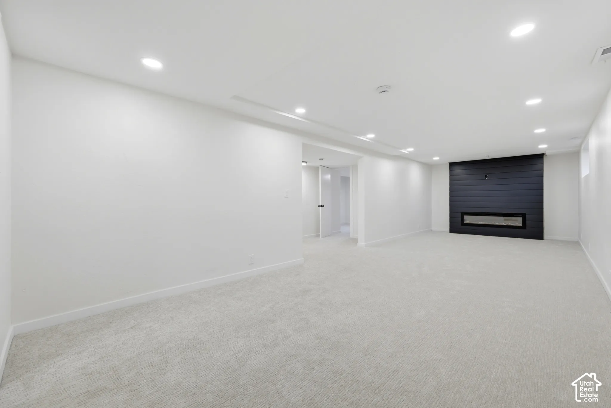 Expansive room featuring recessed lighting, light-colored carpeting, a black horizontal-panel accent wall, and a built-in linear electric fireplace
