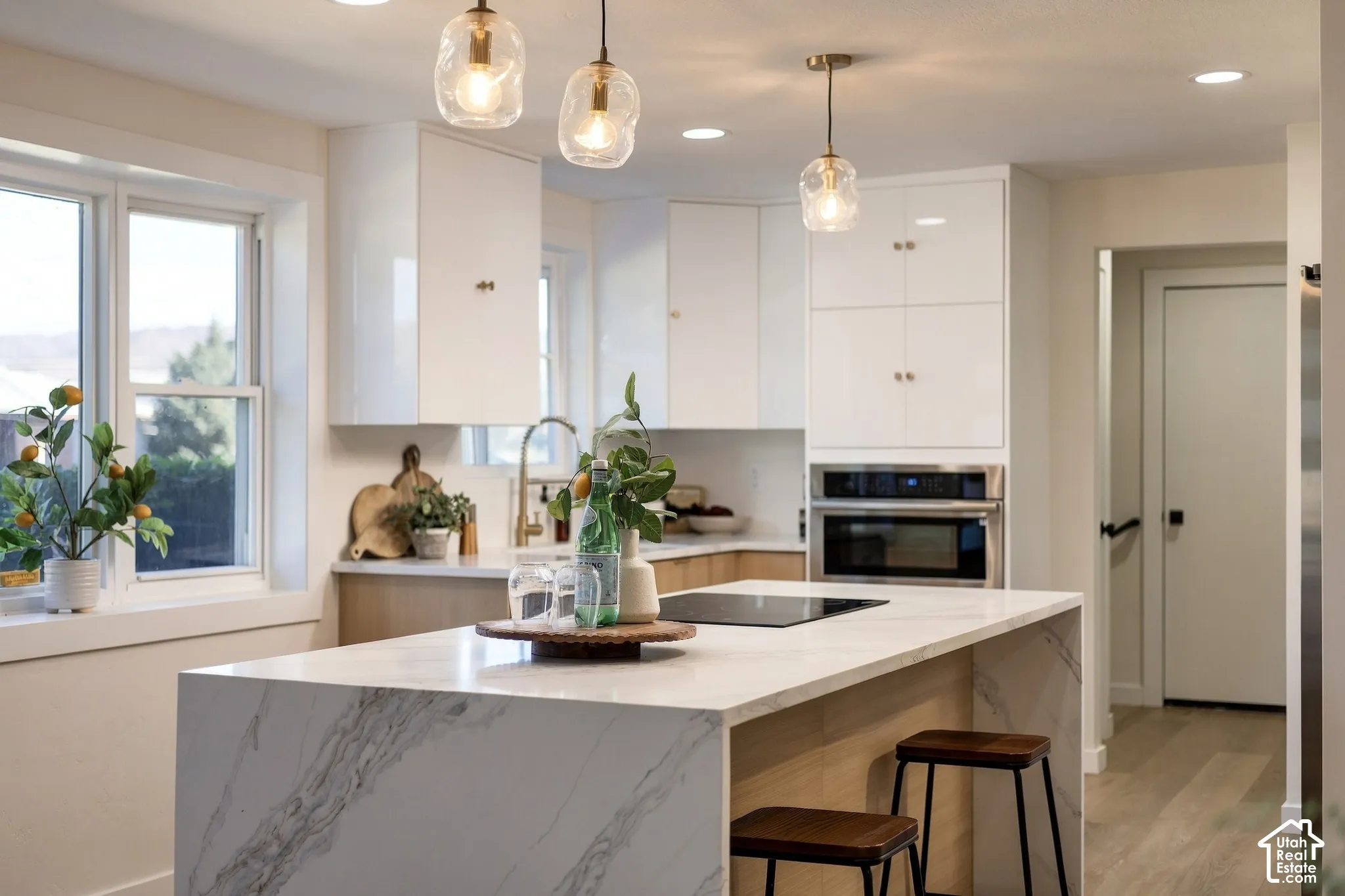 Modern kitchen featuring a waterfall island, built-in stainless steel oven, white cabinetry, and wood-finish flooring