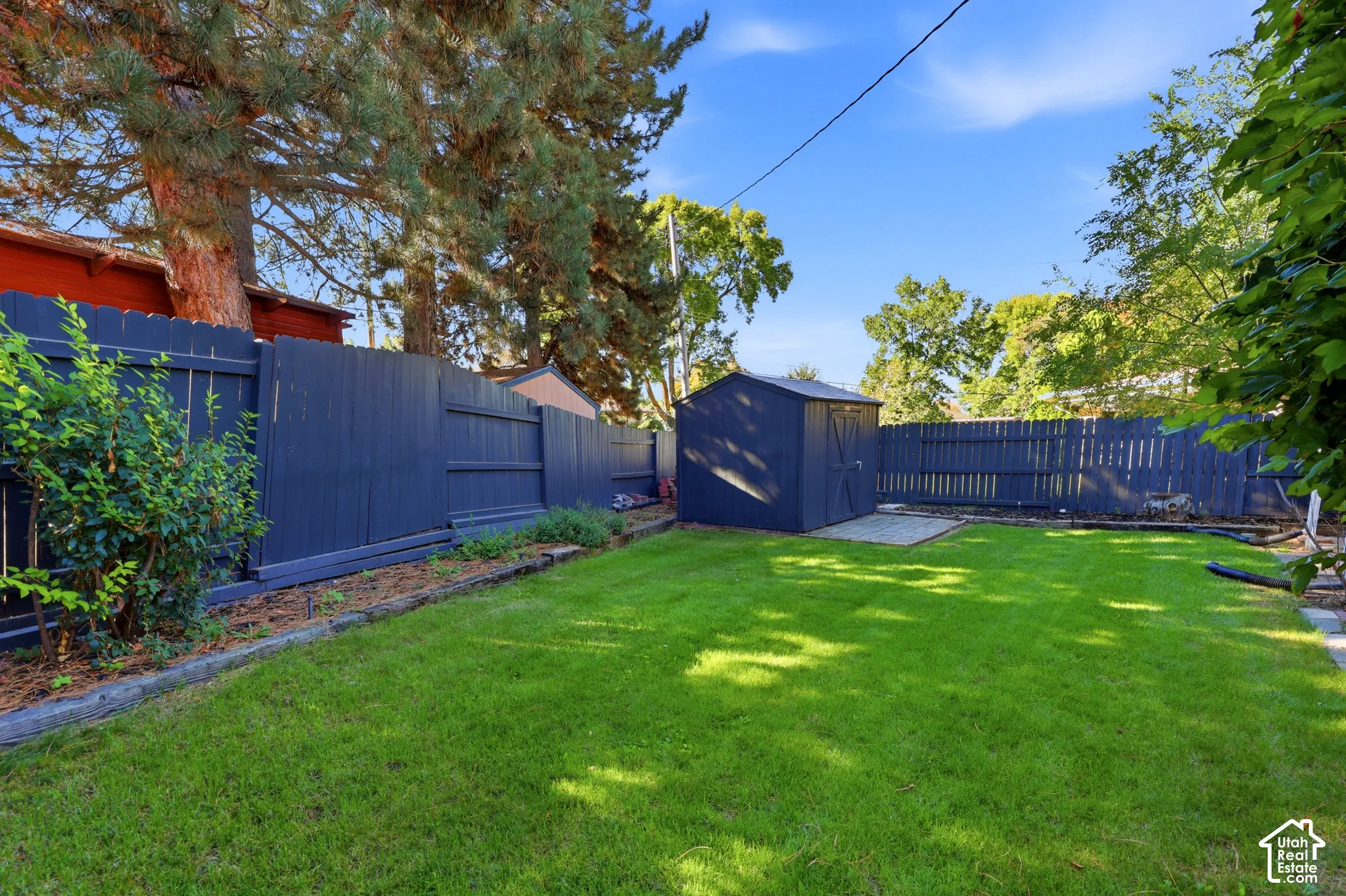 Expansive lawn with a perimeter fence, mature trees, and a detached storage shed on a concrete pad