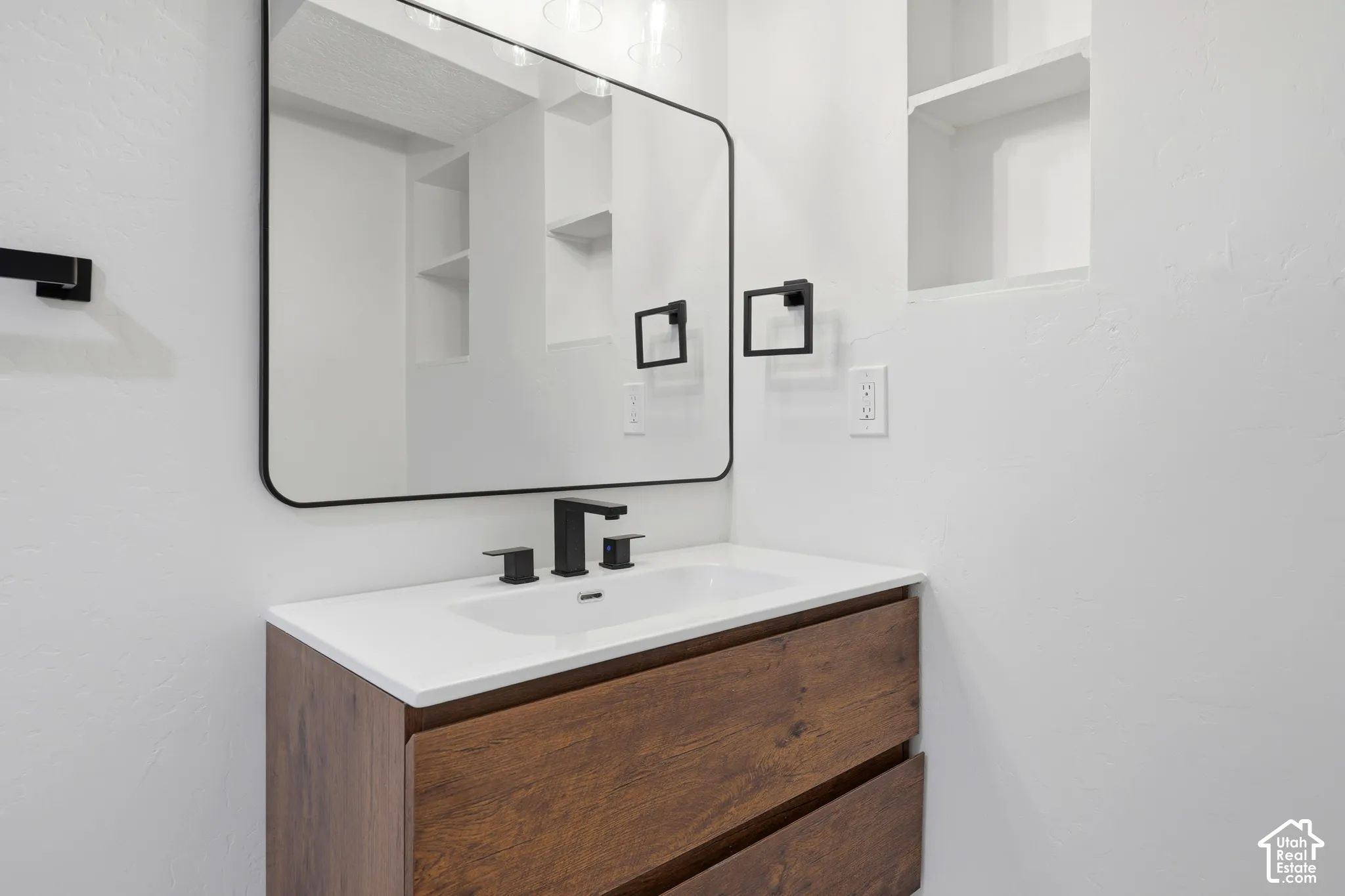 Wood-finish vanity with an integrated sink, matte black faucet, and a rectangular framed mirror