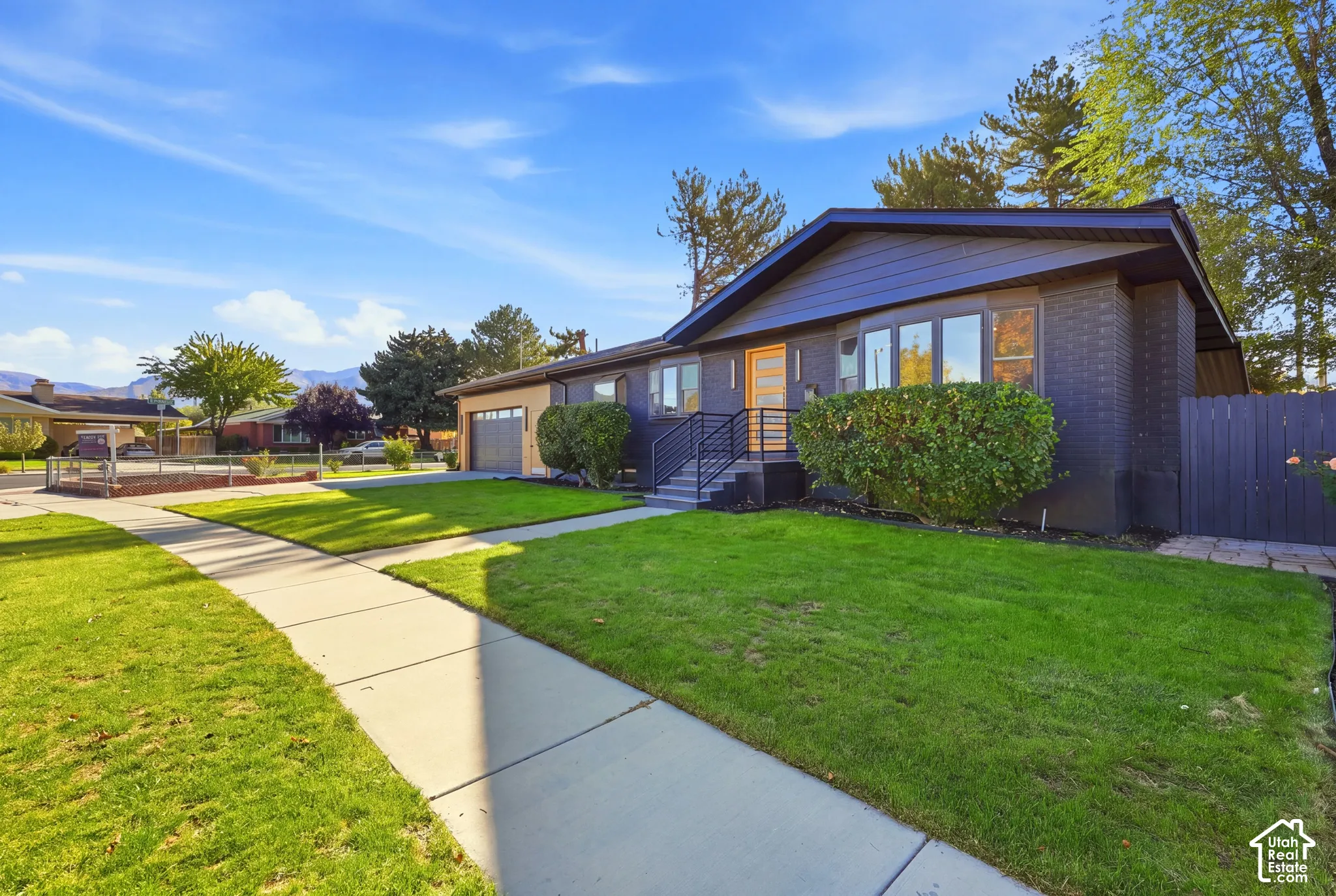 Exterior featuring dark brick facade, light wood-finish front door, front yard with green lawn, and an attached garage