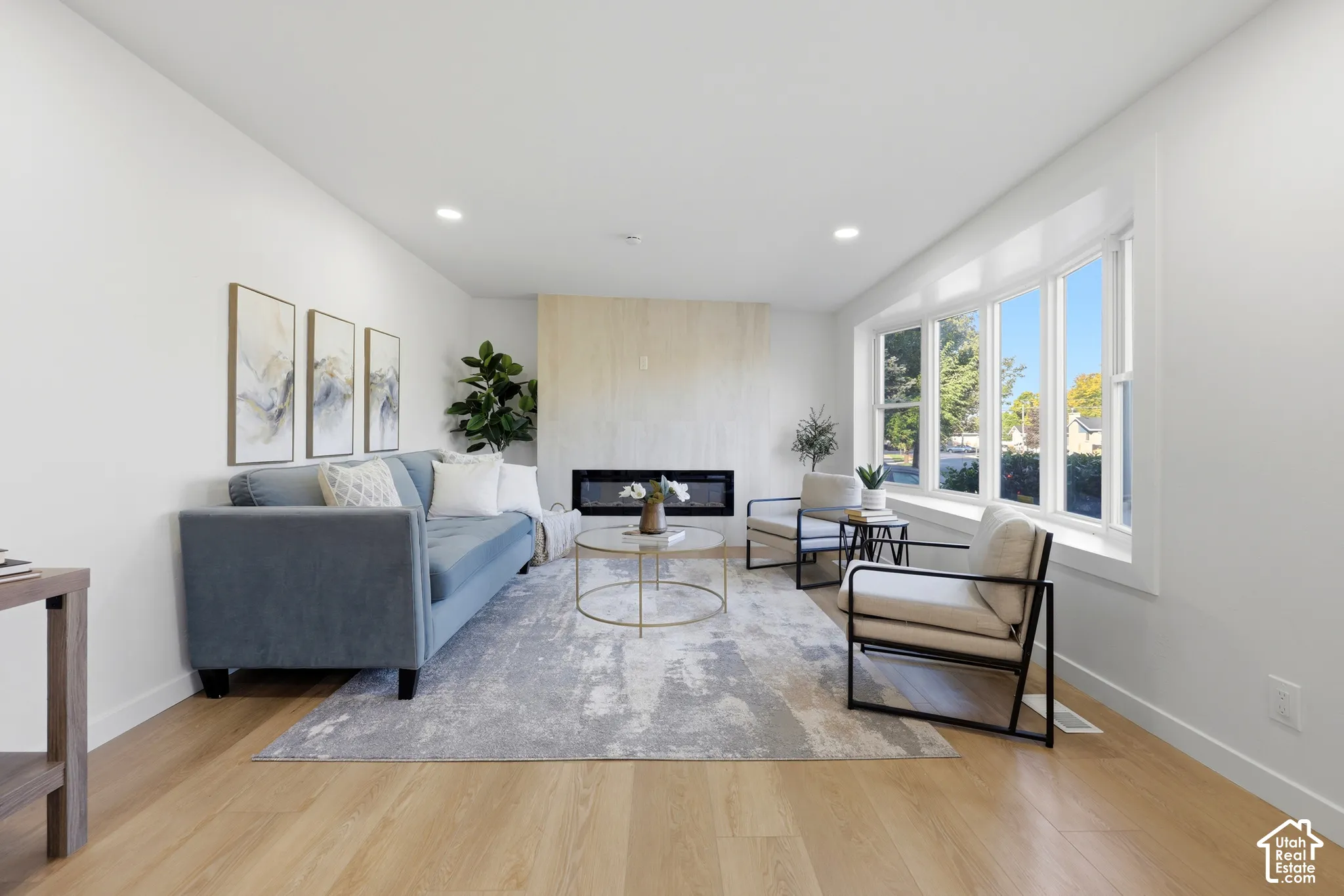 Recessed lighting, wood-finish flooring, bay window, and a built-in linear fireplace with a light-toned surround