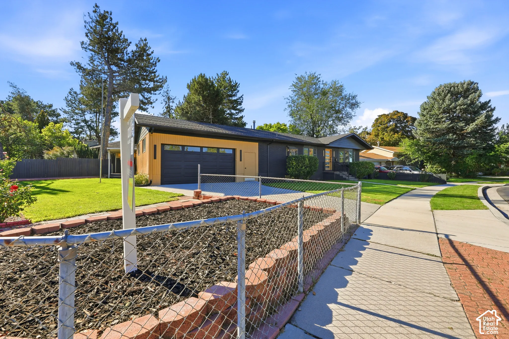 Single-story exterior with a two-car garage, mature trees, a manicured lawn, and a sidewalk