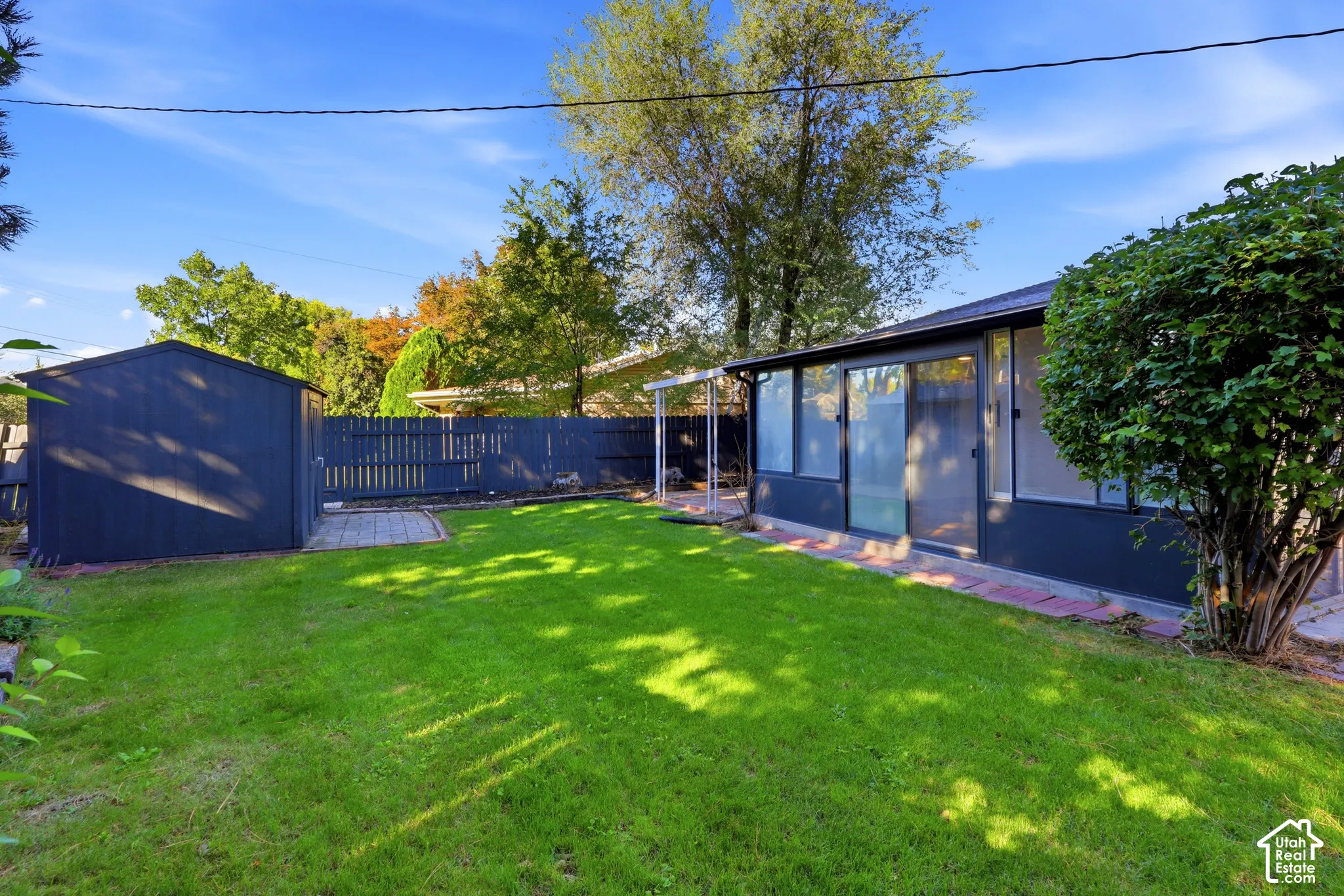 Expansive green lawn, privacy fencing, dedicated storage shed, and a sliding glass door entry to the structure