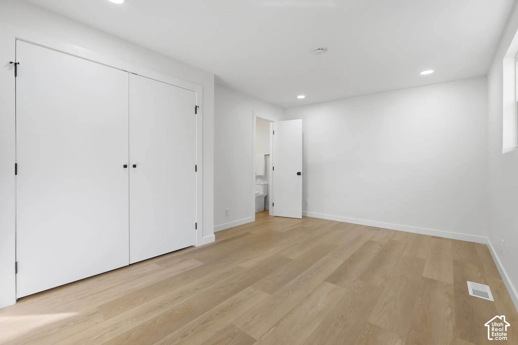Bright, light-filled bedroom featuring gleaming wood-finish flooring, expansive closet storage with dual white panel doors, and recessed ceiling lighting