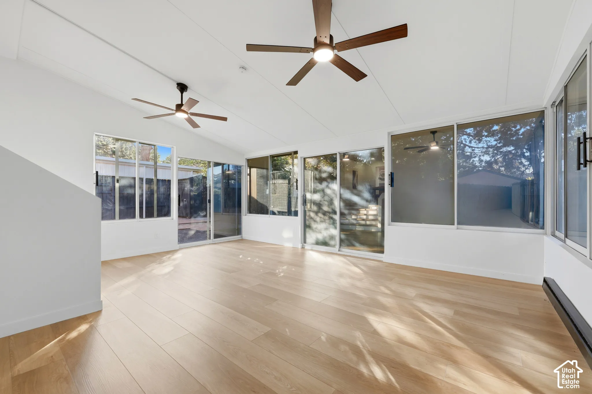 Expansive room with wood-finish flooring, multiple sliding glass doors, white walls, and two ceiling fans