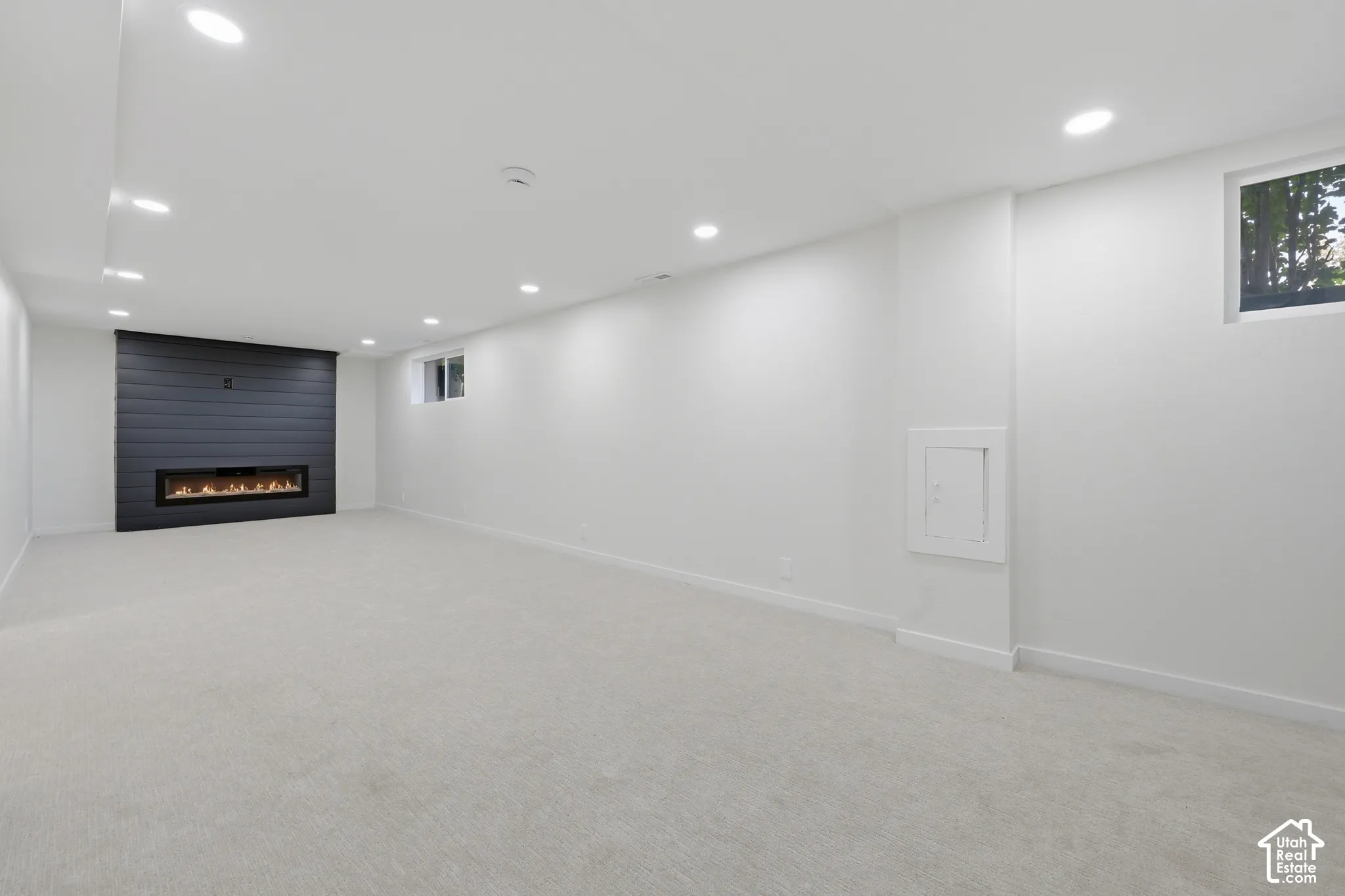 Spacious basement recreation room featuring polished concrete flooring, recessed ceiling lighting, and a modern linear fireplace with dark tile surround