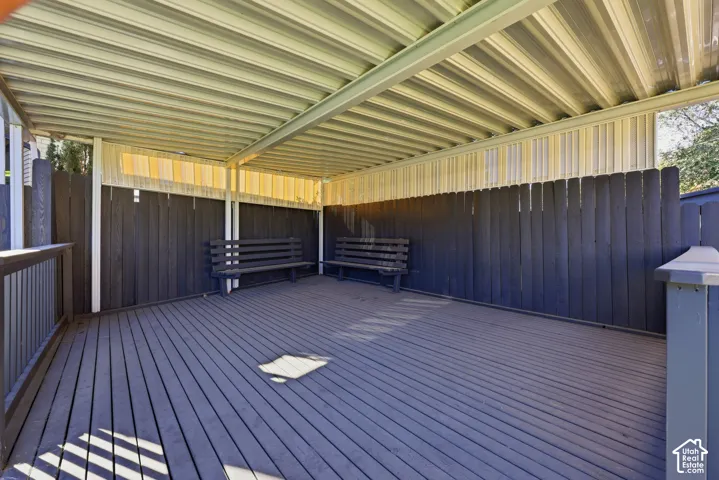 Covered outdoor deck with slatted wood flooring, enclosed by a privacy fence, and featuring a corrugated metal roof