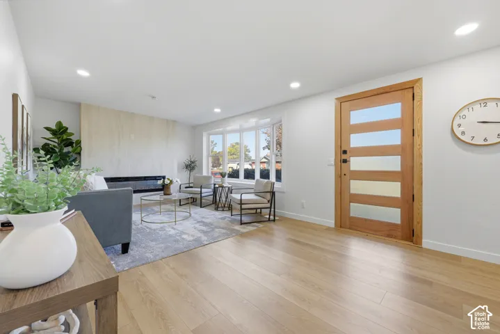 Wood-finish flooring throughout, modern wood-paneled entry door with frosted glass inserts, recessed lighting, expansive bay windows, and a built-in fireplace
