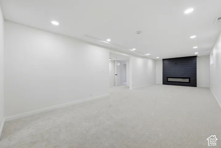 Expansive room featuring recessed lighting, light-colored carpeting, a black horizontal-panel accent wall, and a built-in linear electric fireplace