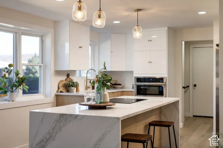 Modern kitchen featuring a waterfall island, built-in stainless steel oven, white cabinetry, and wood-finish flooring