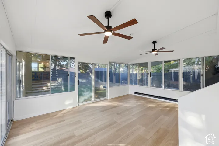 Expansive room featuring wood-finish flooring, multiple sliding glass doors, white vaulted ceilings, and two ceiling fans with integrated lighting