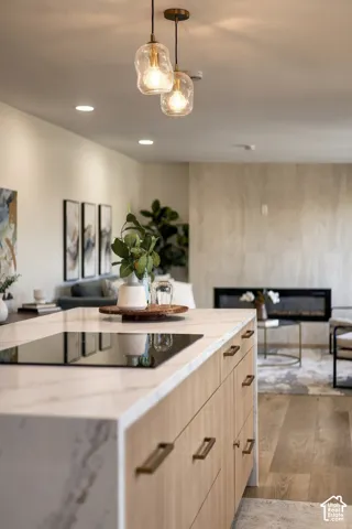 Kitchen island with a waterfall countertop, integrated cooktop, natural wood-finish cabinetry, and bronze hardware