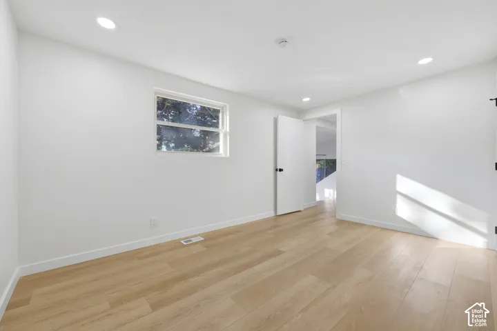 Recessed lighting, wood-finish flooring, white walls, and a white door with black hardware