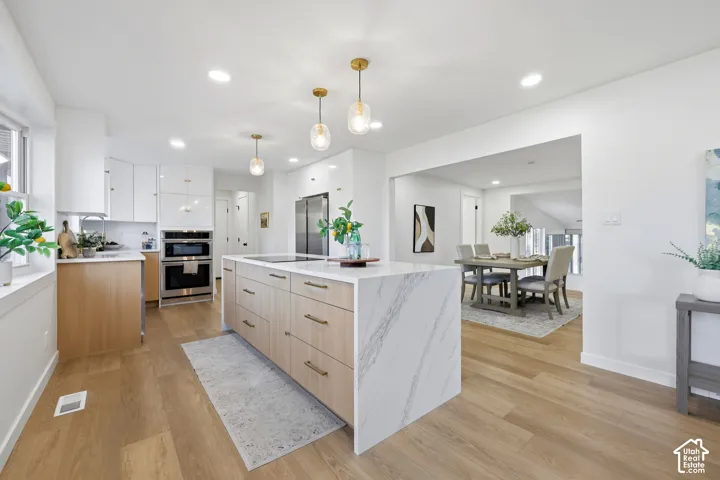 Spacious kitchen featuring an expansive island with a waterfall countertop, wood-finish flooring, recessed lighting, and built-in stainless steel appliances