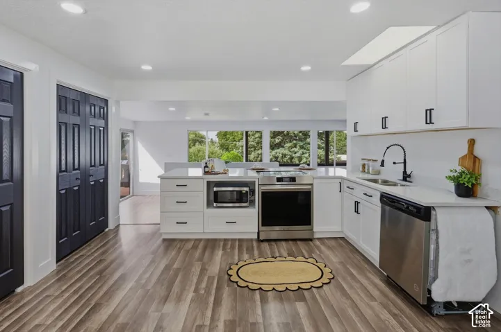 Wood-finish flooring, white cabinetry with matte black hardware, stainless steel appliances, white countertops, and recessed lighting