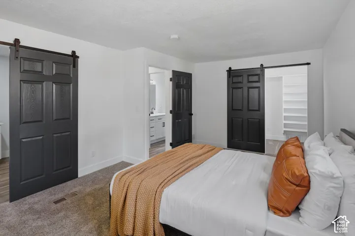 Carpeted flooring, white walls, black barn doors with iron hardware, and built-in shelving