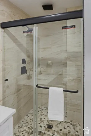 Glass-enclosed shower with matte black hardware, textured tile walls, and a mosaic pebble floor