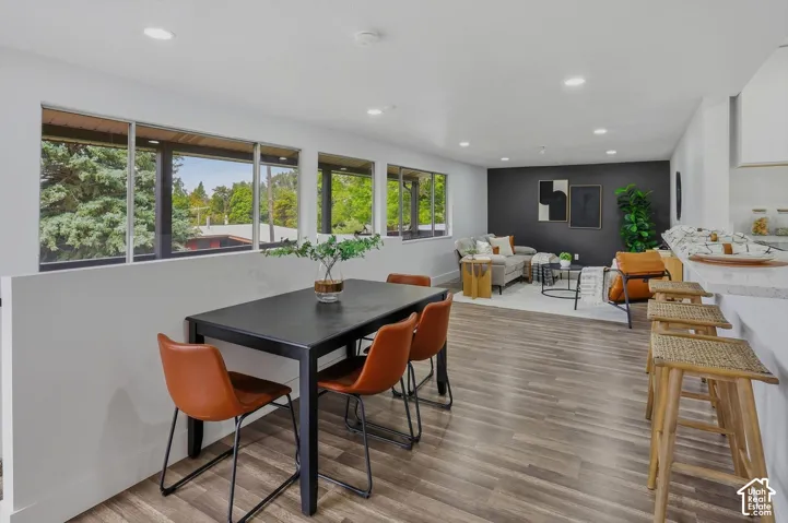 Contemporary dining and kitchen area featuring abundant natural light from expansive multi-pane windows overlooking landscaped grounds, wood-finish flooring throughout, a black dining table with orange upholstered chairs, white cabinetry with integrated a