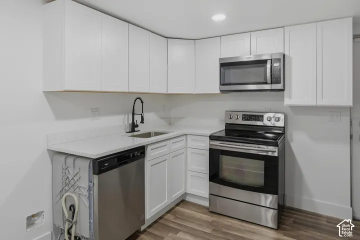 Modern kitchen featuring crisp white cabinetry, stainless steel appliances including a gas range and microwave, quartz countertops, a pull-down faucet with black finish, and wood-finish flooring throughout the space