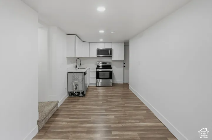Contemporary kitchen featuring wood-finish flooring, white cabinetry, integrated sink with a matte black faucet, and stainless steel appliances