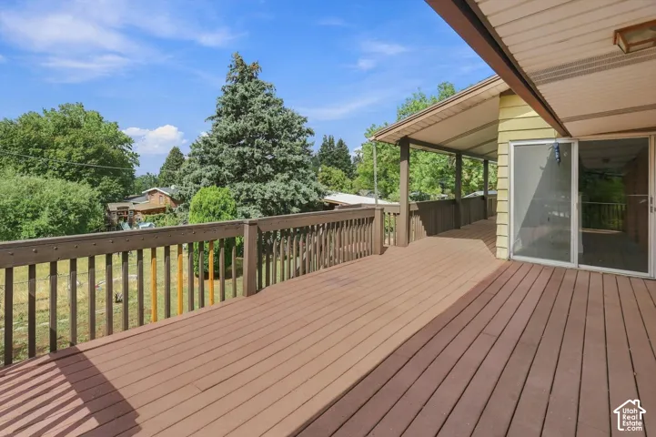 Expansive wood-finish deck with a covered area, a sliding glass door, and a perimeter railing