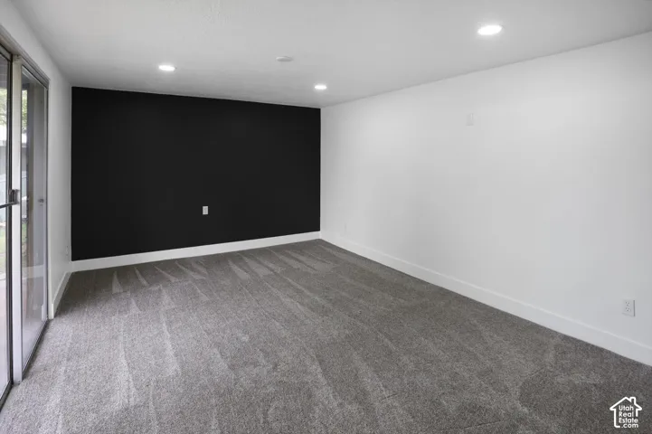 Neutral-toned carpeted room featuring a dark accent wall, recessed lighting, and a sliding glass door