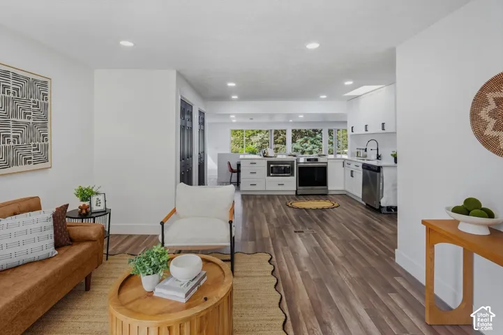 Open-concept living area featuring wood-finish flooring, recessed lighting, and a kitchen with white cabinetry, stainless steel appliances, and a skylight