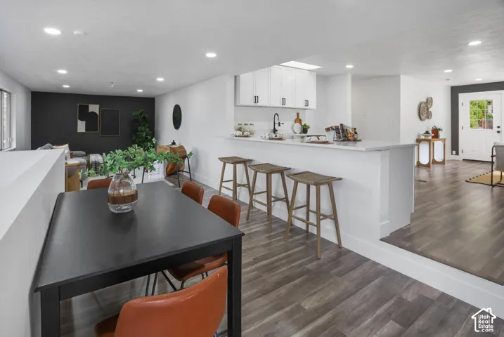 Open-concept living space with wood-finish flooring, recessed lighting, white cabinetry, and a kitchen island with seating