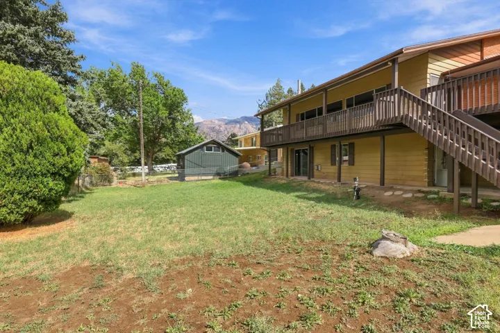 Expansive backyard featuring a green shed, mature trees, and a multi-level deck with wood railing