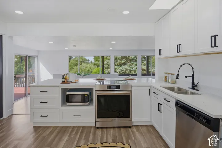 Kitchen featuring white cabinetry, light-colored countertops, stainless steel appliances, and wood-finish flooring