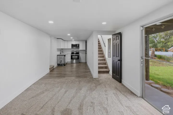 Open-concept living space with recessed lighting, carpeted flooring, and a kitchen area featuring white cabinetry, stainless steel appliances, and wood-finish flooring