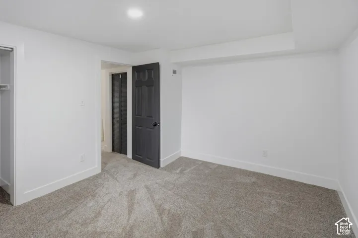 Recessed ceiling lighting, light gray wall-to-wall carpeting, white walls, dark paneled door, and a built-in closet