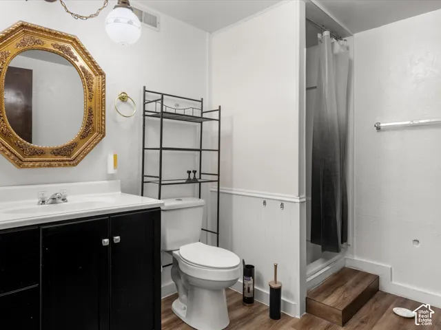 Bathroom featuring wood-finish flooring, white beadboard wainscoting, a vanity with a white countertop, and an elevated shower enclosure