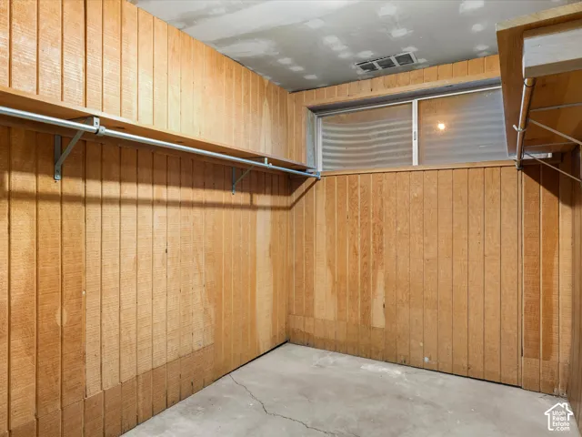 Storage area featuring vertical wood wall paneling, built-in shelving with integrated rods, and a rectangular window