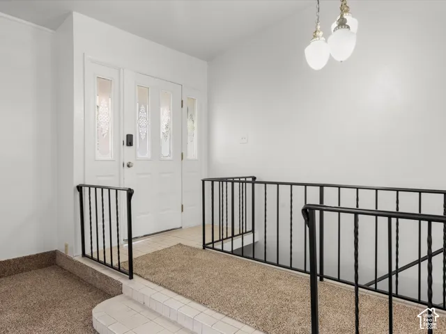 Entryway featuring a white exterior door with decorative glass inserts, black metal railings, and a multi-tiered pendant light fixture