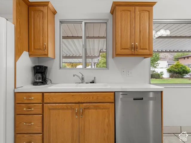 Kitchen featuring shaker-style oak cabinetry, integrated stainless steel dishwasher, white sink with chrome-finish faucet, and solid-surface countertop