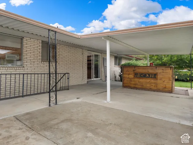 Covered concrete patio featuring light brick exterior, metal support columns, wrought iron railings, and sliding glass door access