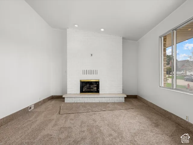 Floor-to-ceiling painted brick fireplace, raised stone hearth, neutral carpeting, and large windows with natural light
