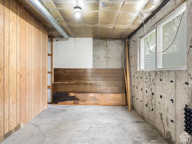 Unfinished space featuring concrete flooring, exposed concrete walls, wood-panel wall accents, and a single-pane window